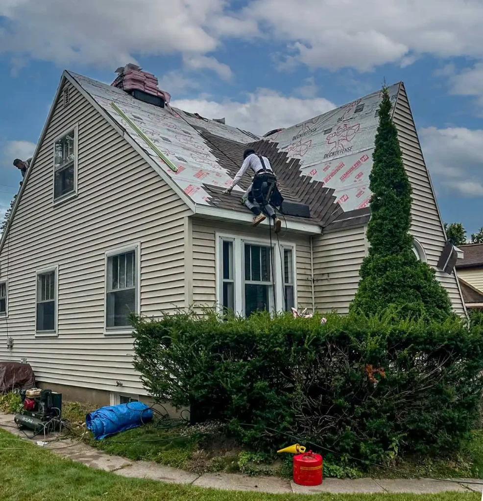 Workers Installing Asphalt Shingles On A Cap Code Style Roof